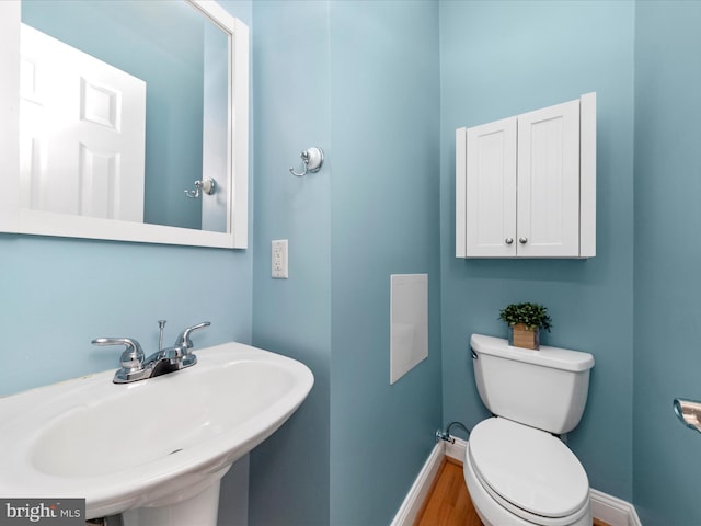 half bath with toilet, wood finished floors, baseboards, and a sink