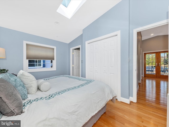 bedroom with baseboards, lofted ceiling with skylight, light wood-type flooring, french doors, and a closet