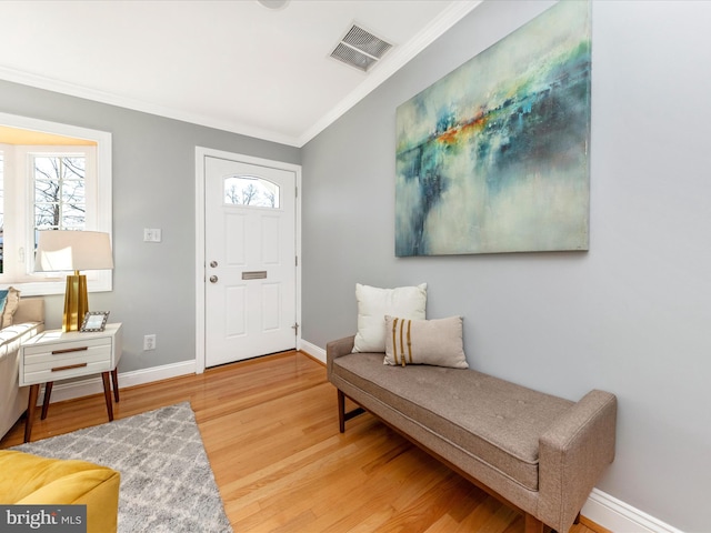 foyer featuring light wood finished floors, visible vents, baseboards, and ornamental molding