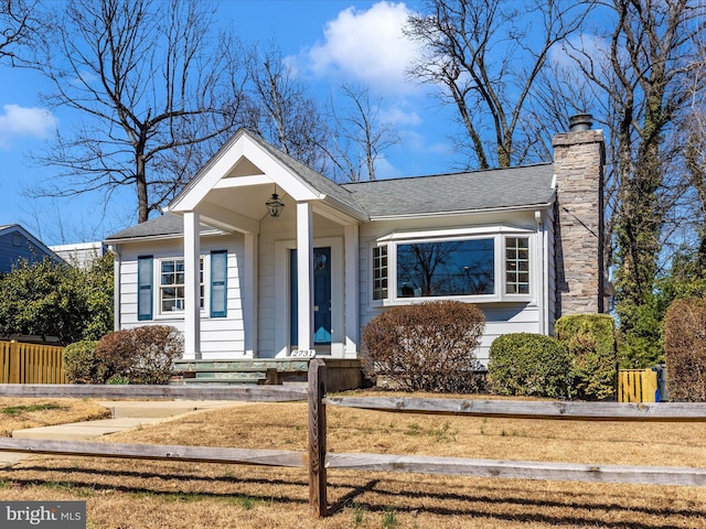 bungalow-style home featuring a fenced front yard, a chimney, and a shingled roof