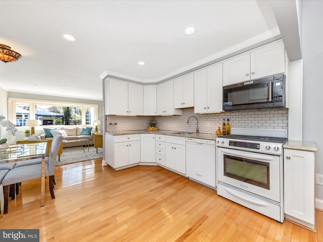 kitchen featuring tasteful backsplash, light wood-type flooring, ornamental molding, white appliances, and a sink