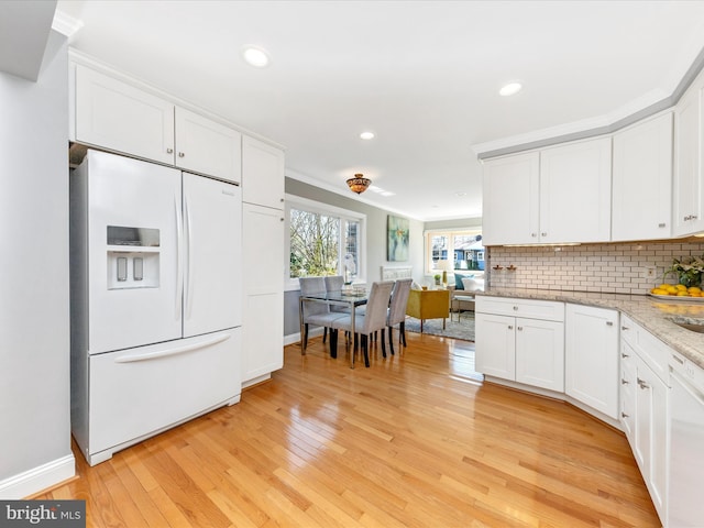 kitchen with white appliances, light wood-style floors, white cabinets, decorative backsplash, and light stone countertops