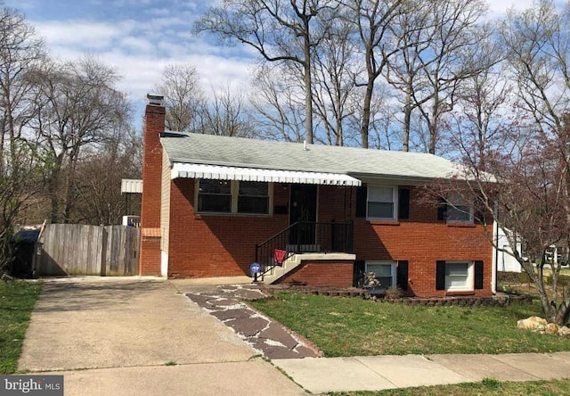 view of front of home featuring brick siding, fence, a chimney, and a front lawn