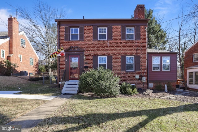 view of front of property with brick siding, a front lawn, and a chimney