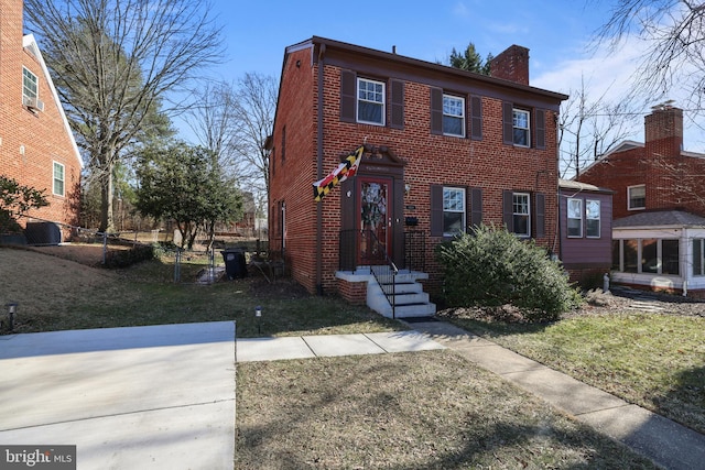 view of front of home featuring brick siding, a chimney, a front yard, and fence