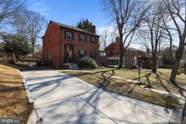 colonial home featuring brick siding, a chimney, and a front lawn