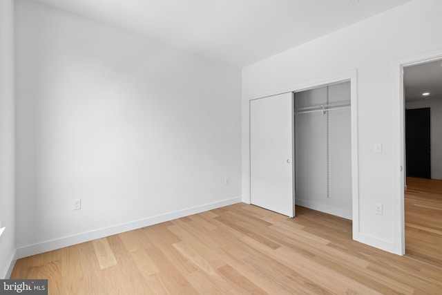 unfurnished bedroom with light wood-type flooring, baseboards, and a closet