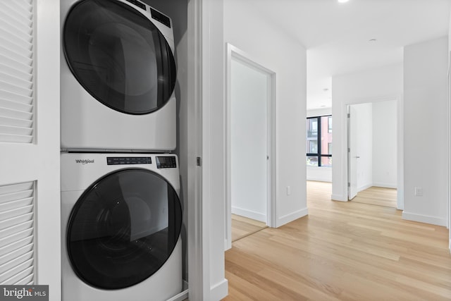 clothes washing area with stacked washer and dryer, laundry area, baseboards, and light wood finished floors