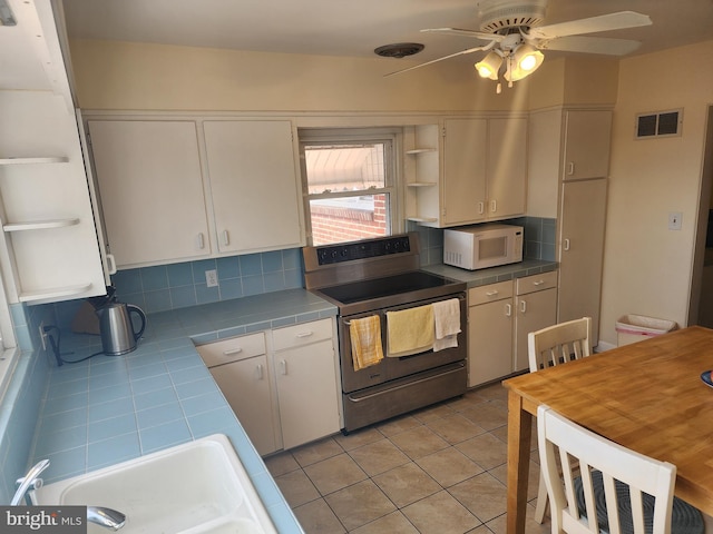 kitchen with electric range, visible vents, tile countertops, white microwave, and open shelves