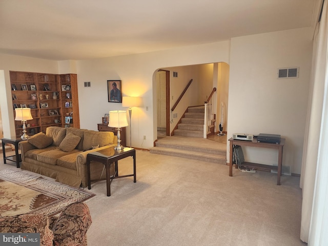 living area featuring stairs, visible vents, and light colored carpet