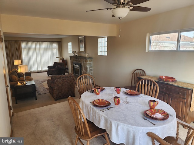 carpeted dining space featuring a ceiling fan and a stone fireplace