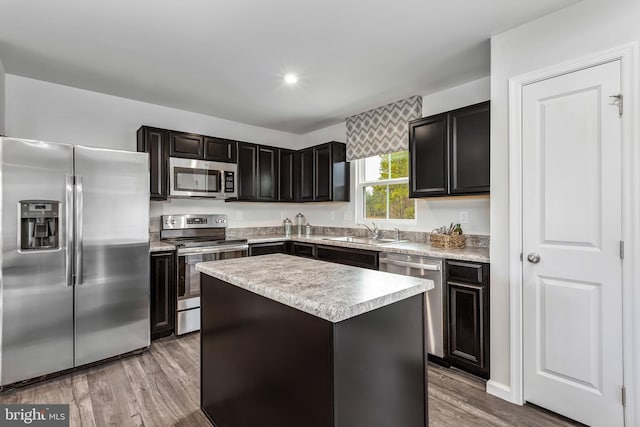 kitchen featuring wood finished floors, appliances with stainless steel finishes, a kitchen island, and a sink