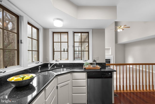 kitchen with dark stone counters, a fireplace, stainless steel dishwasher, white cabinetry, and a sink