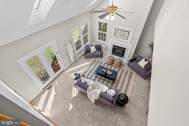 carpeted living room with a high end fireplace, a skylight, high vaulted ceiling, and a ceiling fan