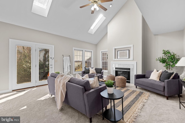 living area with carpet flooring, high vaulted ceiling, a skylight, and a tiled fireplace