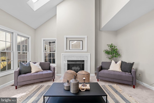 living area featuring baseboards, a premium fireplace, light carpet, a skylight, and high vaulted ceiling