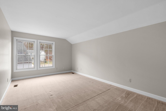 carpeted spare room featuring visible vents, lofted ceiling, and baseboards