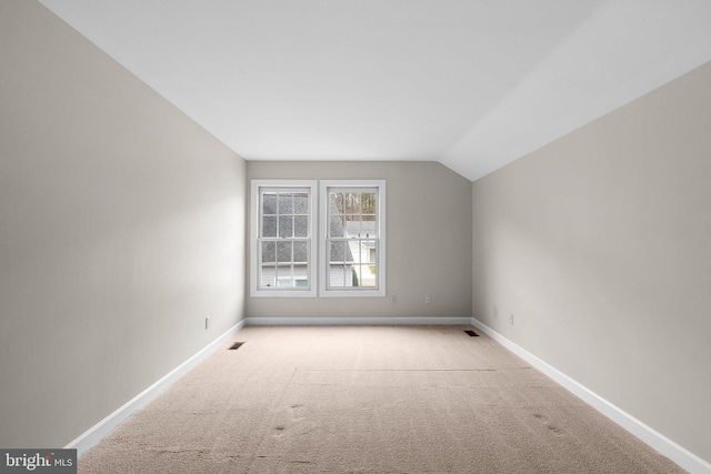 carpeted empty room featuring visible vents, baseboards, and vaulted ceiling