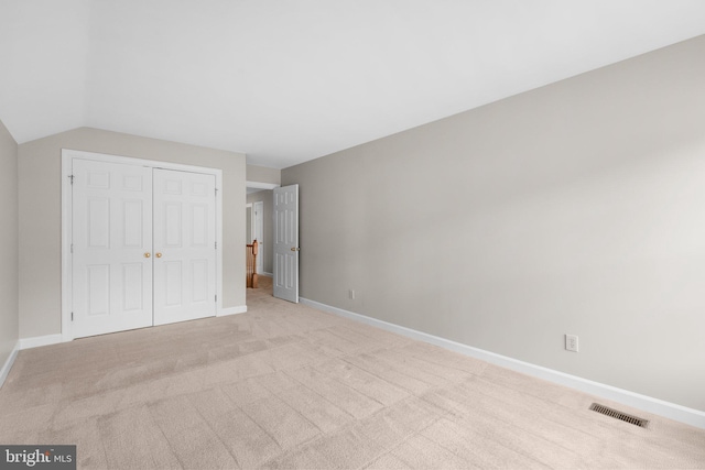 unfurnished bedroom featuring visible vents, lofted ceiling, a closet, baseboards, and light colored carpet