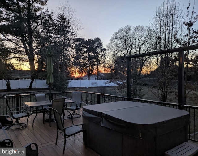 deck at dusk with outdoor dining space, fence, and a hot tub