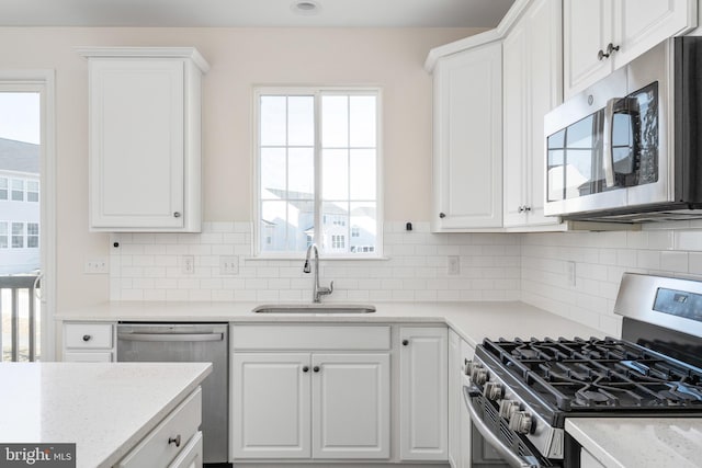 kitchen featuring decorative backsplash, appliances with stainless steel finishes, white cabinets, and a sink