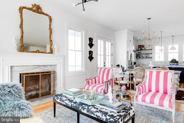 living area featuring light wood-style floors, a high end fireplace, a chandelier, and french doors