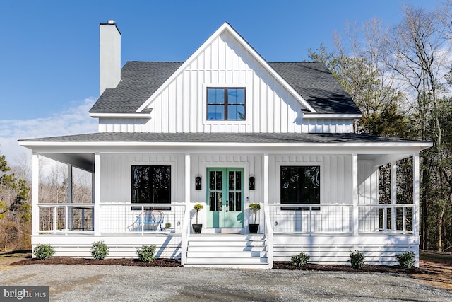 view of front of house with covered porch, a shingled roof, french doors, board and batten siding, and a chimney