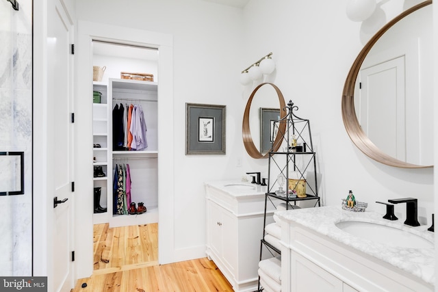 full bathroom with a spacious closet, wood finished floors, two vanities, and a sink