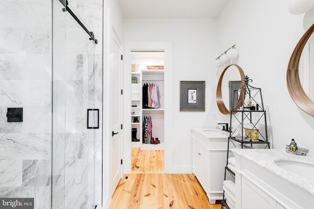 full bath featuring a marble finish shower, two vanities, wood finished floors, a walk in closet, and a sink