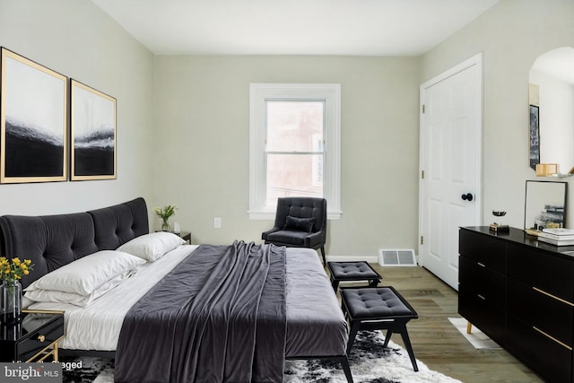 bedroom with arched walkways, wood finished floors, visible vents, and baseboards