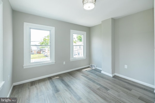 empty room with wood finished floors, visible vents, and baseboards