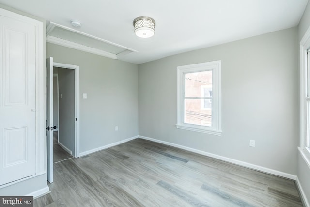 unfurnished room with wood finished floors, attic access, and baseboards