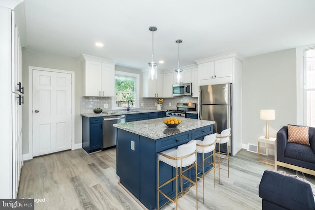 kitchen with light wood-style flooring, a breakfast bar, white cabinetry, appliances with stainless steel finishes, and tasteful backsplash