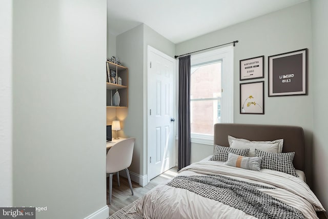 bedroom featuring light wood-type flooring, built in study area, and baseboards