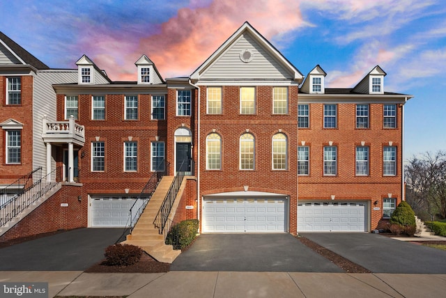 view of property with an attached garage, stairs, aphalt driveway, and brick siding