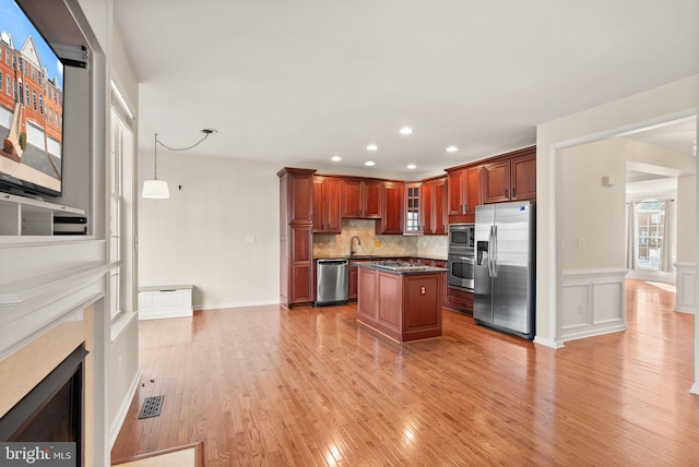 kitchen with light wood finished floors, a kitchen island, glass insert cabinets, appliances with stainless steel finishes, and backsplash