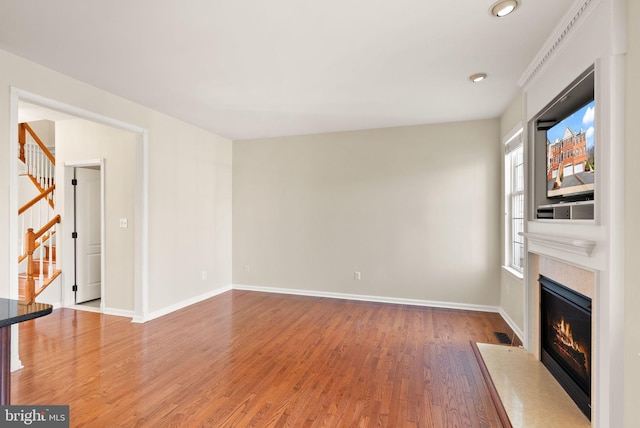 unfurnished living room featuring a fireplace with flush hearth, stairs, baseboards, and wood finished floors