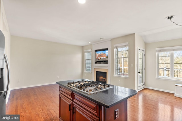 kitchen featuring light wood finished floors, a warm lit fireplace, baseboards, appliances with stainless steel finishes, and open floor plan