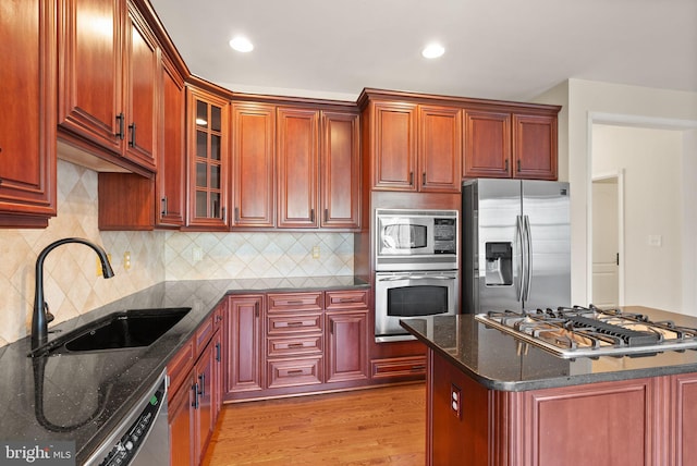 kitchen featuring glass insert cabinets, dark stone countertops, stainless steel appliances, light wood-style floors, and a sink