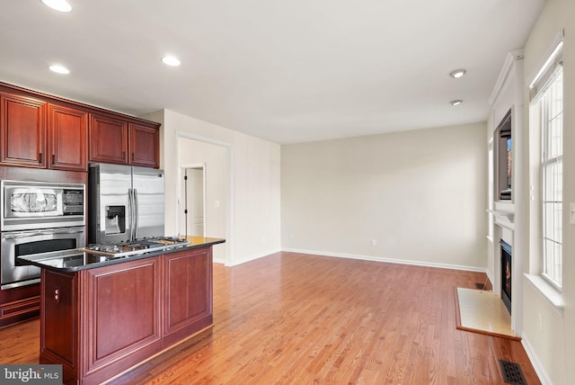 kitchen featuring stainless steel appliances, light wood finished floors, a fireplace with flush hearth, and dark brown cabinets