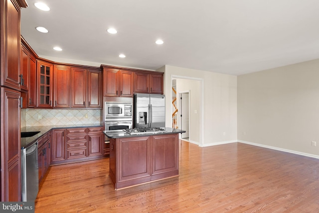 kitchen featuring stainless steel appliances, a kitchen island, light wood-style floors, tasteful backsplash, and glass insert cabinets