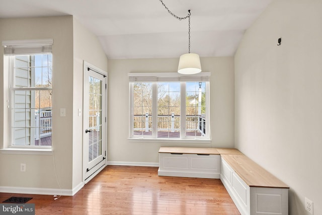 unfurnished dining area with lofted ceiling, light wood-type flooring, visible vents, and baseboards