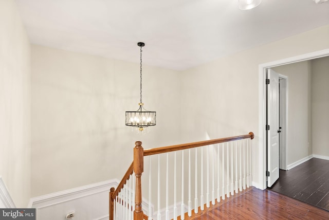 corridor with baseboards, wood finished floors, an upstairs landing, and a notable chandelier