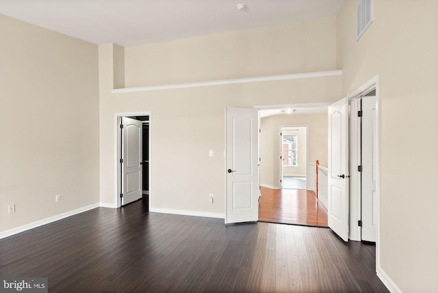 spare room with a towering ceiling, dark wood finished floors, visible vents, and baseboards