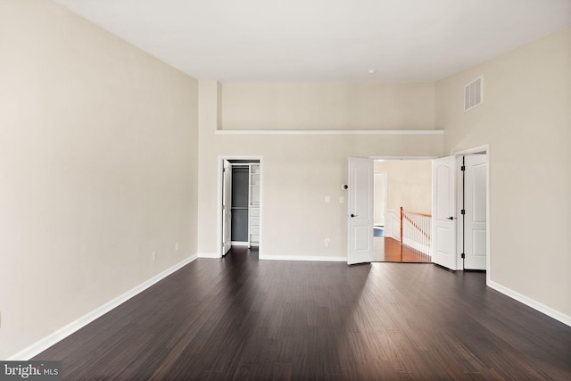 unfurnished room with dark wood-style floors, a high ceiling, visible vents, and baseboards