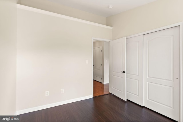 unfurnished bedroom with a closet, baseboards, and dark wood-type flooring