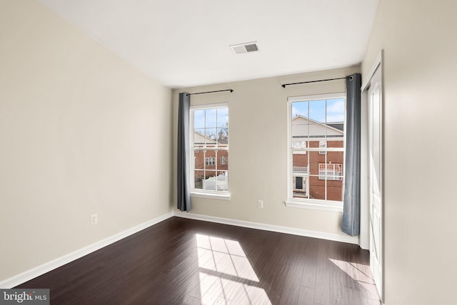 empty room with dark wood-type flooring, visible vents, and baseboards