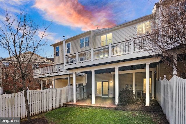 back of house at dusk with a patio area, a fenced backyard, and a balcony