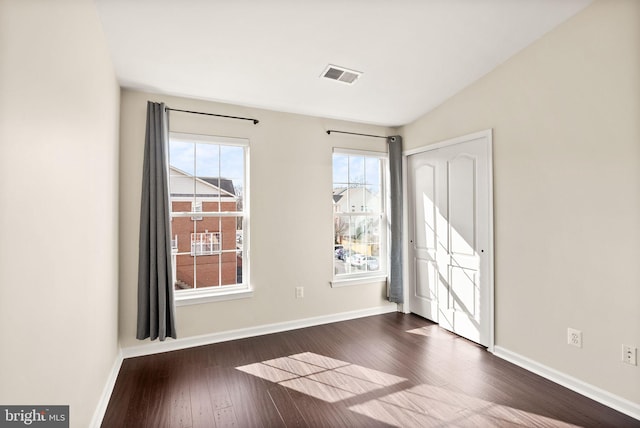 spare room featuring baseboards, visible vents, dark wood finished floors, and a wealth of natural light