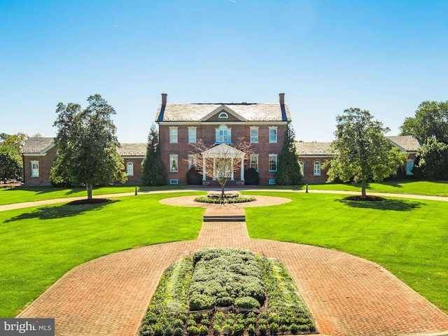 colonial home featuring brick siding, decorative driveway, and a front yard